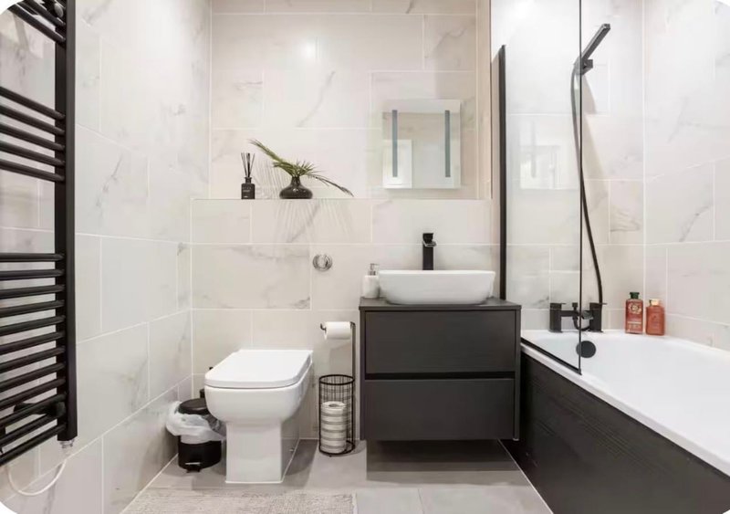 Modern bathroom with white marble tiles, black vanity, vessel sink and bathtub