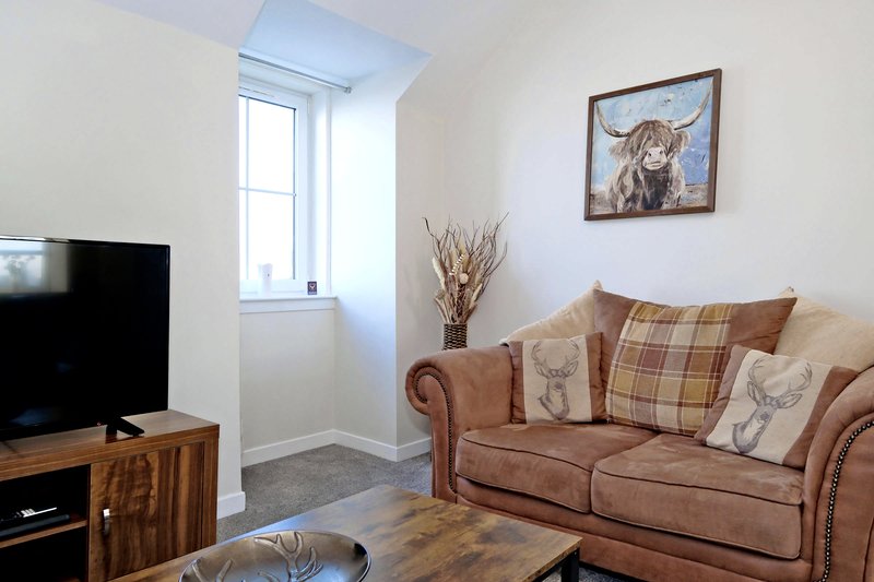 Living room with brown sofa, wooden TV stand, window, and framed wall art