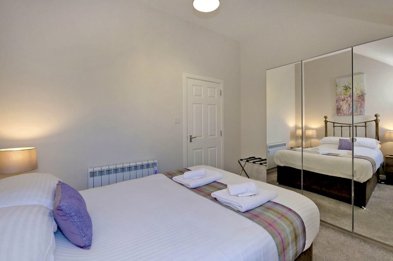 Bright bedroom with double bed, purple cushion, mirrored wardrobe and en-suite visible