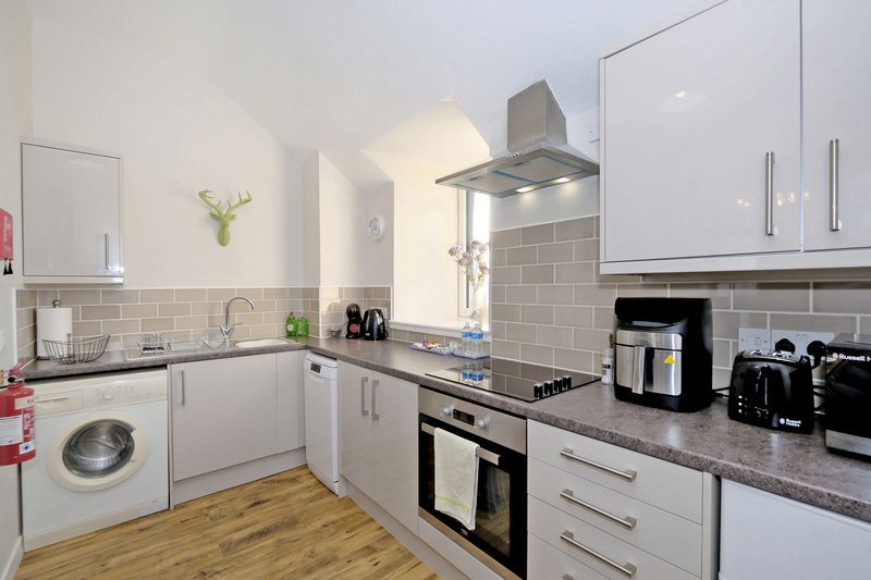 Modern kitchen with white cabinets, black countertops, stainless steel appliances and wooden flooring