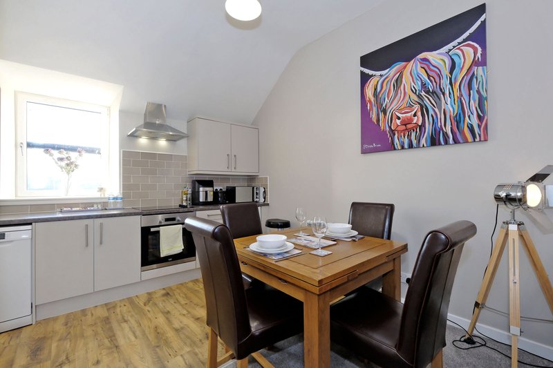Kitchen-diner with white cabinetry, wooden dining table, brown chairs and colorful wall art
