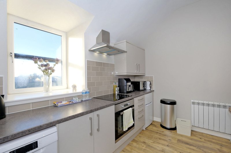 Modern white kitchen with gray countertop, built-in appliances and window overlooking landscape