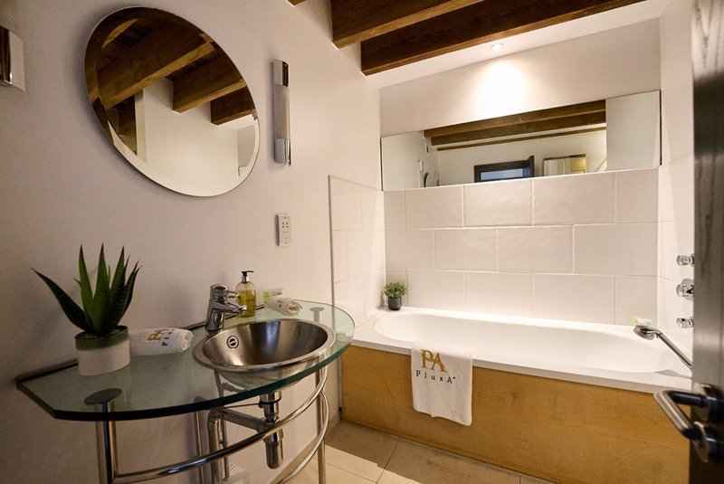 Modern bathroom with bathtub, round mirror, pedestal sink, and potted plant