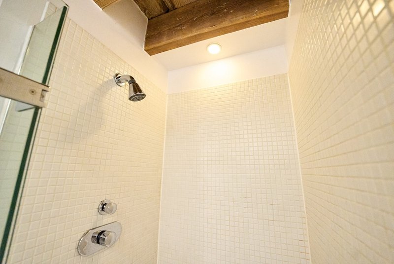 Modern bathroom shower enclosure with white tile walls and wooden ceiling beam