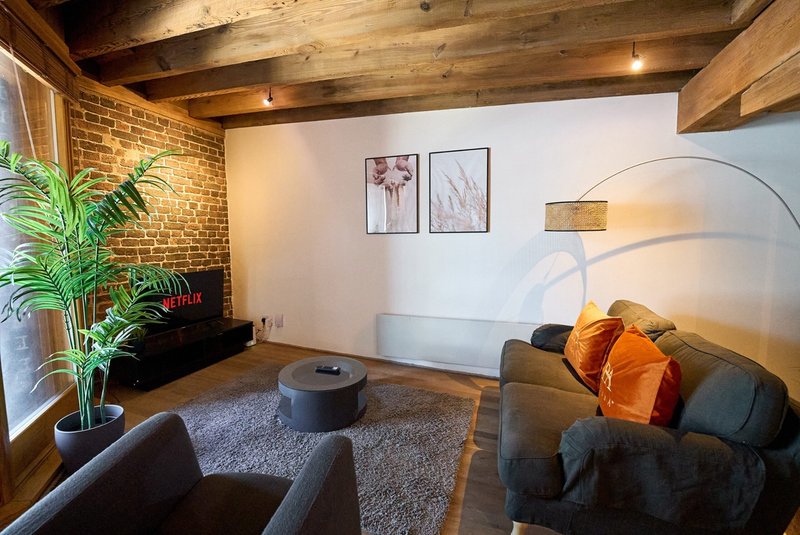 Modern loft living room with exposed brick, wooden beams, dark sofa and orange cushions