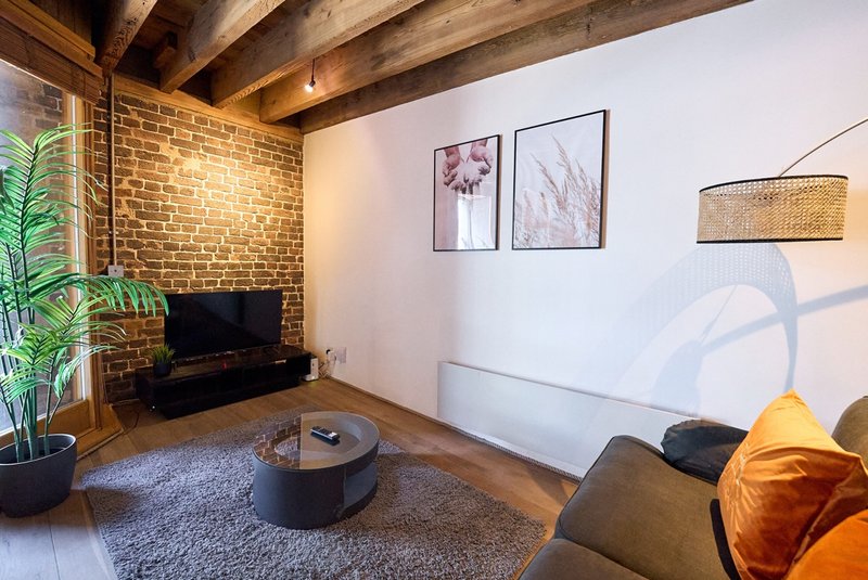 Living room with exposed brick, wooden beams, fireplace, and modern seating furniture