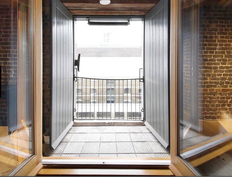Industrial brick balcony with metal railing, glass doors, and tiled flooring