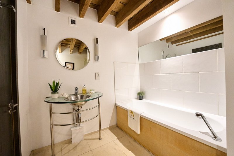 Bathroom with bathtub, round mirror, small sink console table and wooden beams