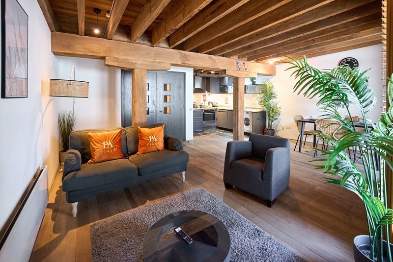 Open-plan living room with dark sofa, wooden beams, potted plants and modern furnishings