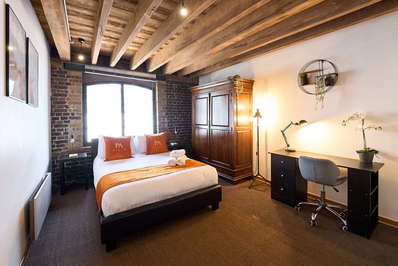 Modern bedroom with queen bed, wooden beams, brick wall, desk area and pendant lighting