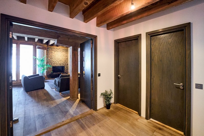 Modern hallway with wooden flooring, dark doors, and view into furnished living room