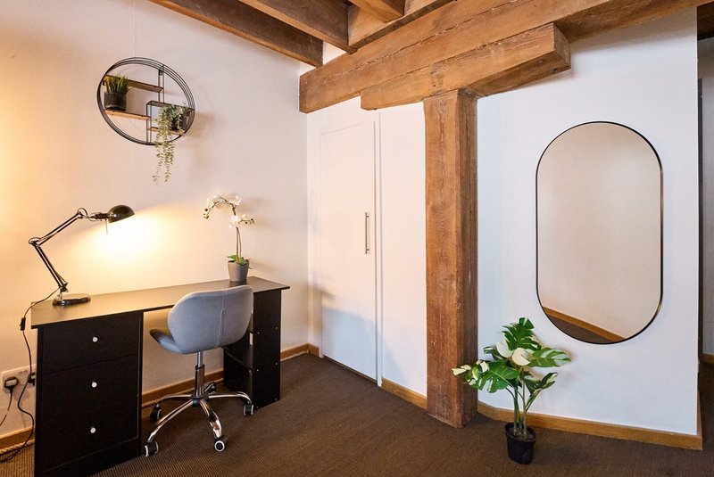 Modern workspace with black desk, desk lamp, office chair, wooden beams and mirrors