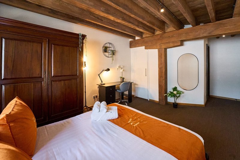 Spacious bedroom with wooden beams, orange and white bedding, dark wood wardrobe and desk area