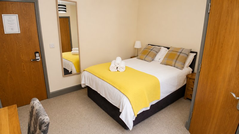 Bedroom with double bed, yellow bedspread, white pillows, mirror and wooden doors