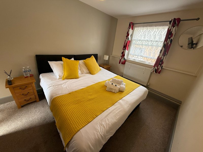 Bright bedroom with double bed, yellow bedding, wooden nightstand and purple curtains