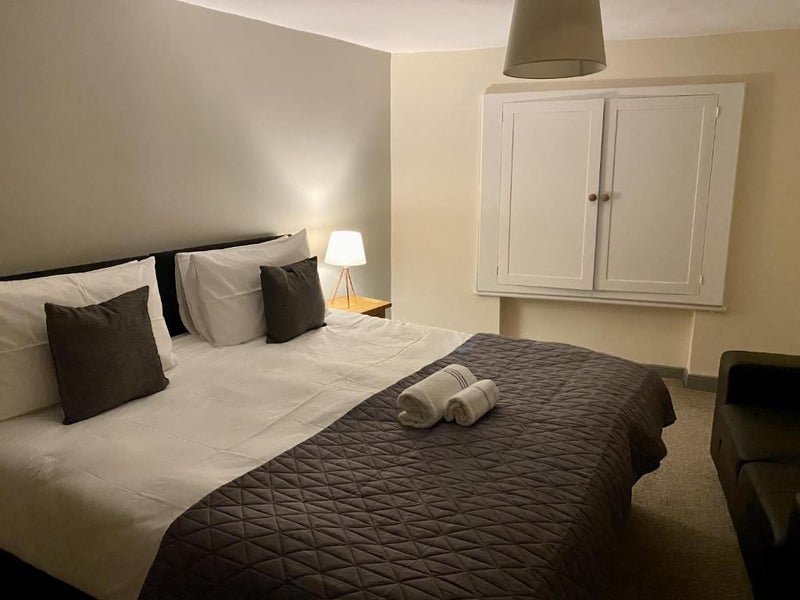 Modern bedroom with double bed, black headboard, white pillows and dark throw, white wall cabinet