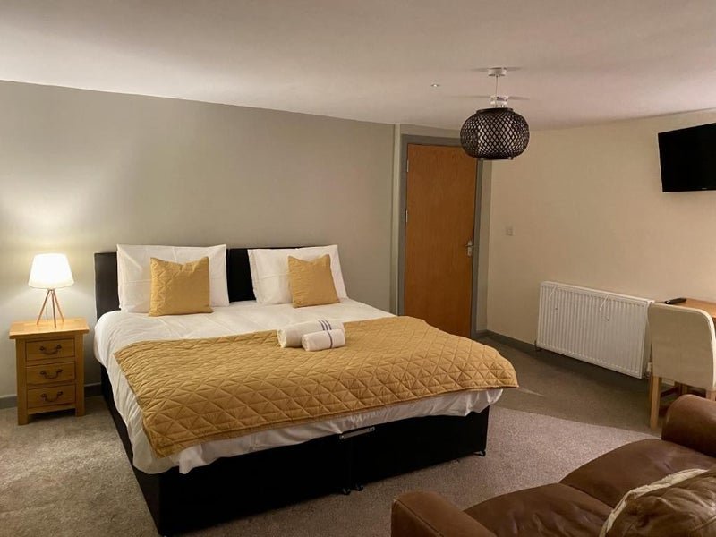 Spacious bedroom with queen bed, gold bedding, wooden nightstand, pendant light, and TV on wall