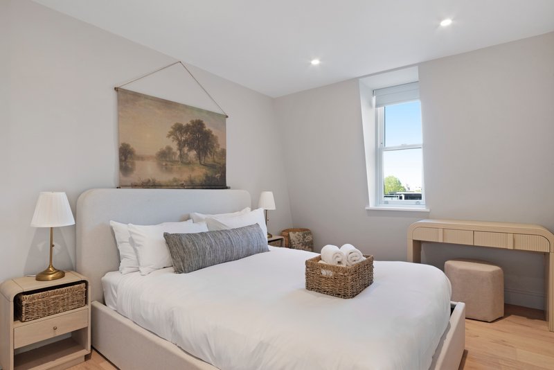 Bright bedroom with queen bed, bedside lamps, wooden furniture and framed landscape artwork