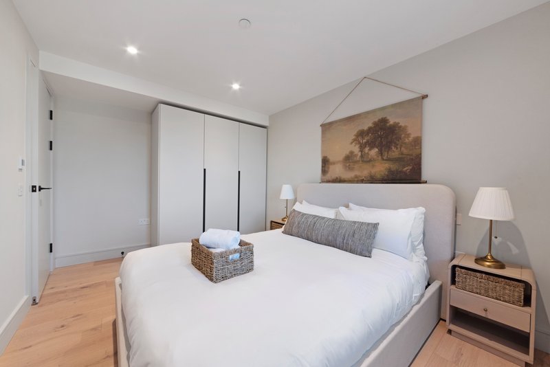 Modern bedroom with queen bed, gray headboard, wooden nightstand, and framed landscape artwork