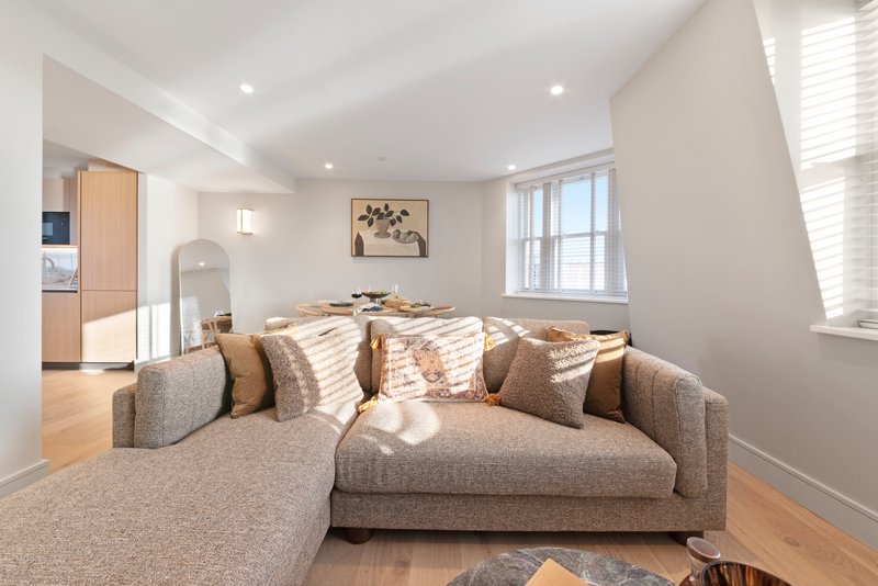Bright open-plan living room with beige corner sofa, wooden flooring, and large windows