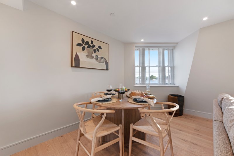Modern dining area with round wooden table, two chairs, and window overlooking city