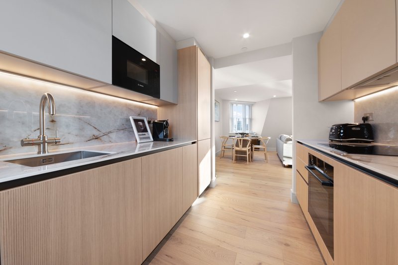 Modern galley kitchen with light wood cabinetry, stainless steel appliances, and open plan dining area