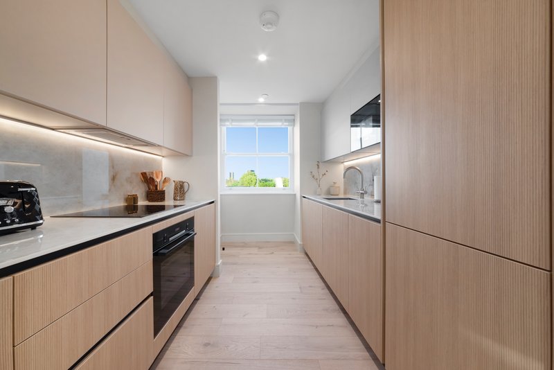 Modern galley kitchen with wooden cabinets, stainless steel appliances and window overlooking garden