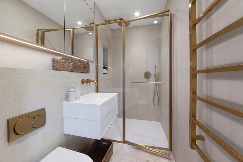 Modern bathroom with white vanity, brass fixtures, walk-in shower and heated towel rack