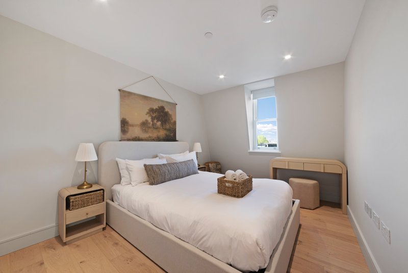 Bright bedroom with double bed, wooden nightstand, wall art, and window with natural light