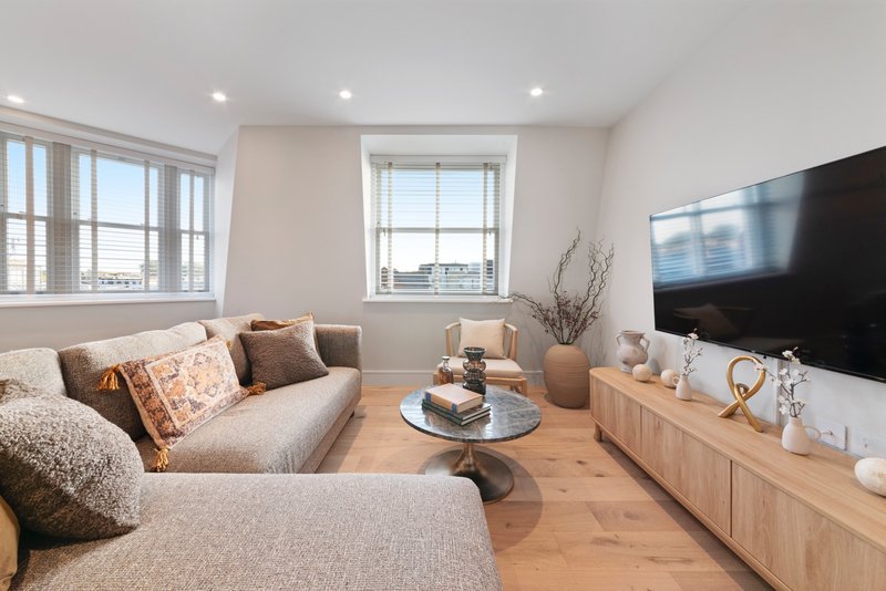 Modern living room with beige corner sofa, wooden TV unit, and large windows with city views