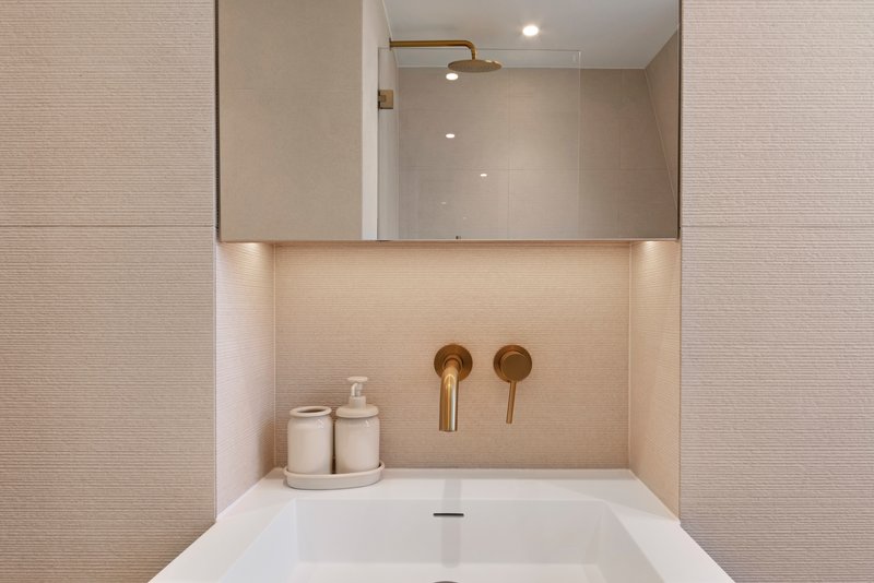 Modern bathroom sink with mirror, cream toiletries, and brass wall fixtures