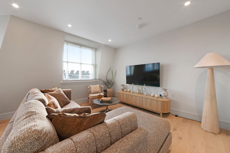 Modern living room with beige sofa, wooden TV stand, flat-screen TV, and floor lamp
