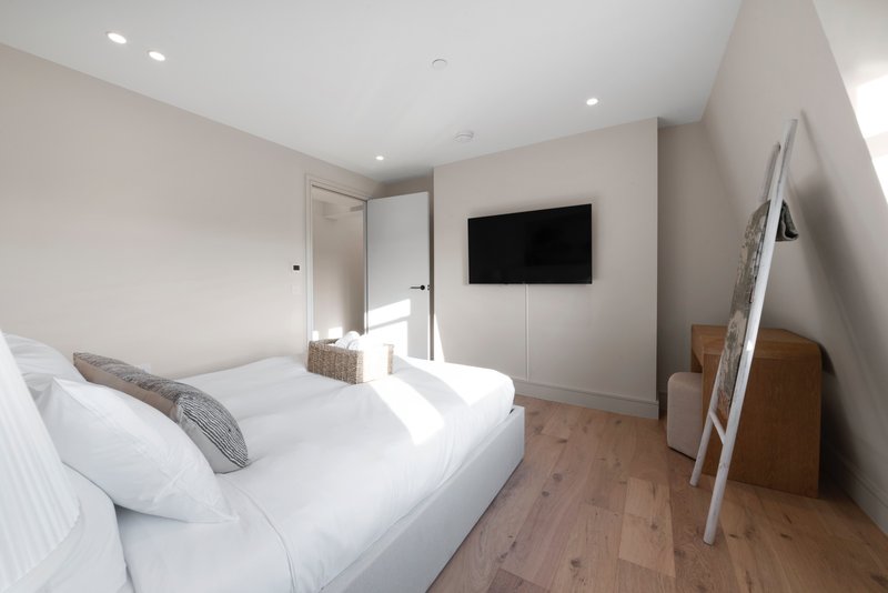 Modern bedroom with white bed, wall-mounted TV, wooden floor and ensuite bathroom