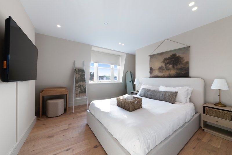 Modern bedroom with queen bed, wall-mounted TV, wooden floor and natural light