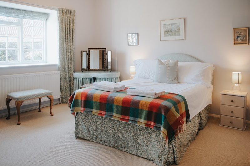 Bright bedroom with double bed, colorful plaid throw, bedside table and window with curtains