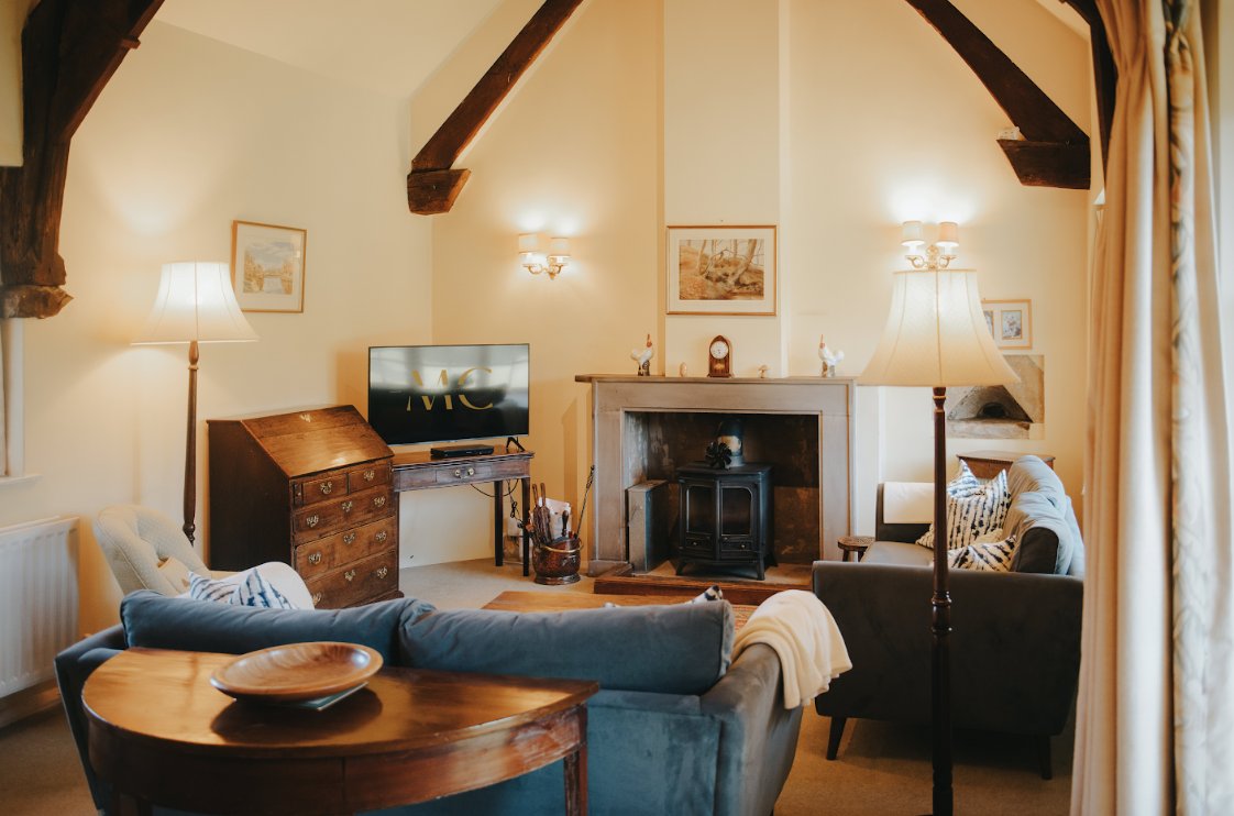 Bright living room with exposed beams, wood stove, blue sofa, wooden table and lamps