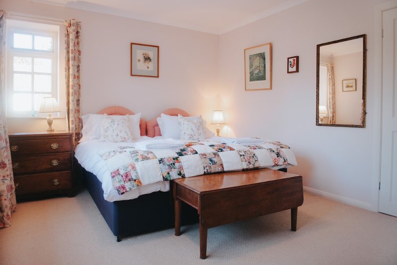 Bright bedroom with two single beds, wooden furniture, framed wall art and window with floral curtains