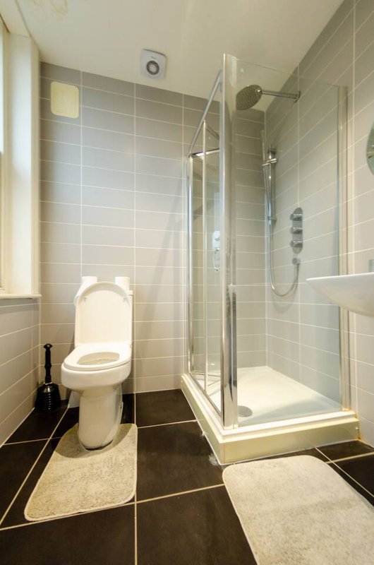 Modern bathroom with toilet, walk-in shower, tiled walls and dark floor