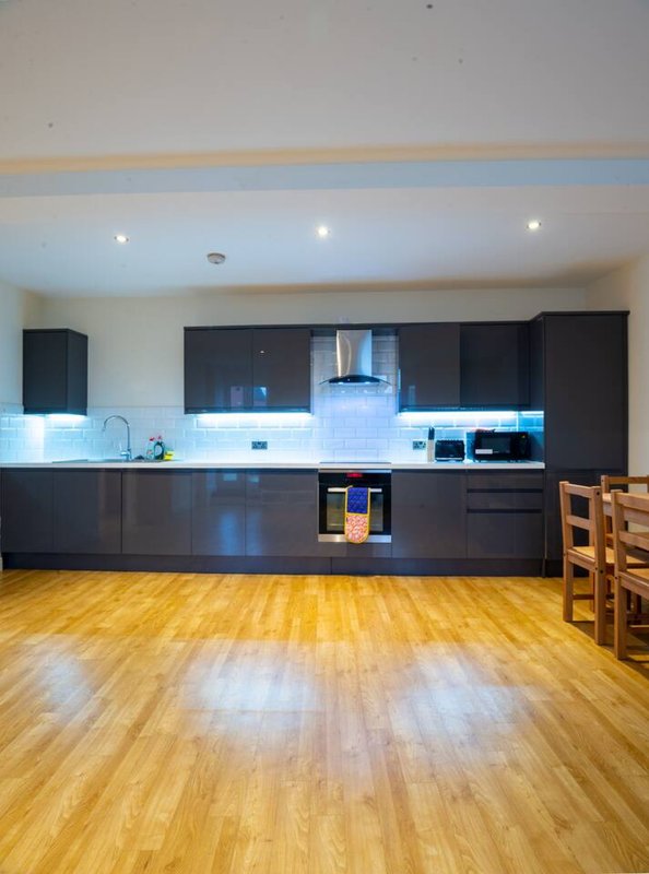 Modern kitchen with dark cabinetry, white splashback, wooden flooring and dining chairs