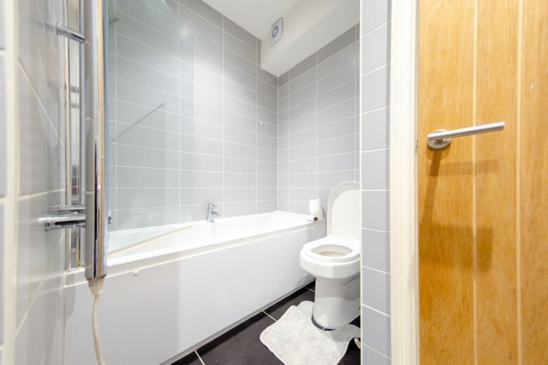 Modern bathroom with white bathtub, glass shower screen, toilet and grey tile walls