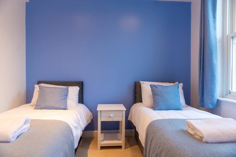 Bedroom with two single beds, blue accent wall, bedside table and window