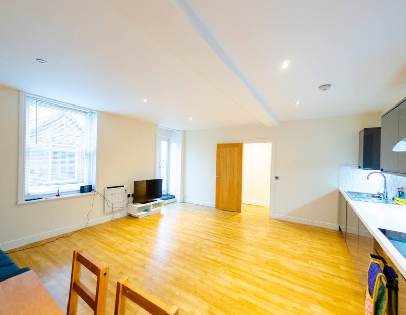 Open-plan living space with wooden flooring, kitchen area, and bright windows