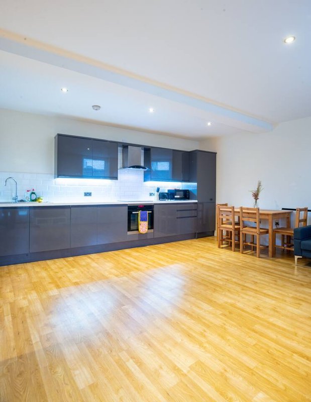 Modern open-plan kitchen and dining area with dark cabinetry, wooden flooring and dining table