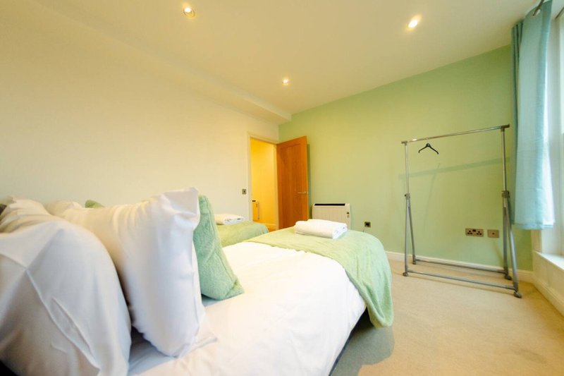 Bright bedroom with double bed, green accent wall, ensuite bathroom with glass partition