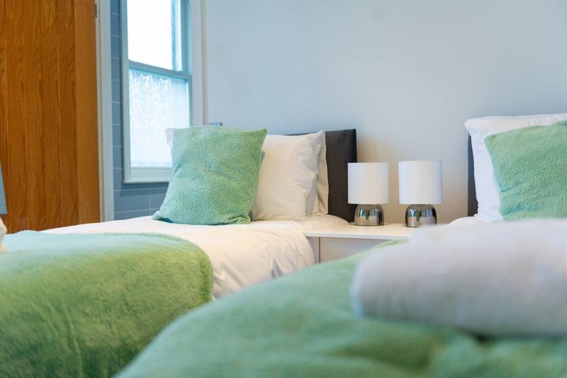 Bright bedroom with twin beds, green and cream cushions, wooden door and window