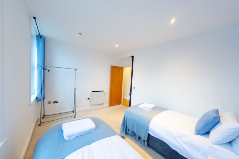 Modern bedroom with two single beds, blue throws, ensuite bathroom with glass shower screen