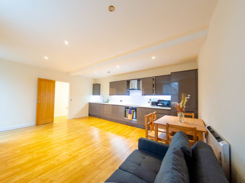 Open-plan living area with wooden flooring, dark sofa, dining table and modern kitchen with dark cabinetry