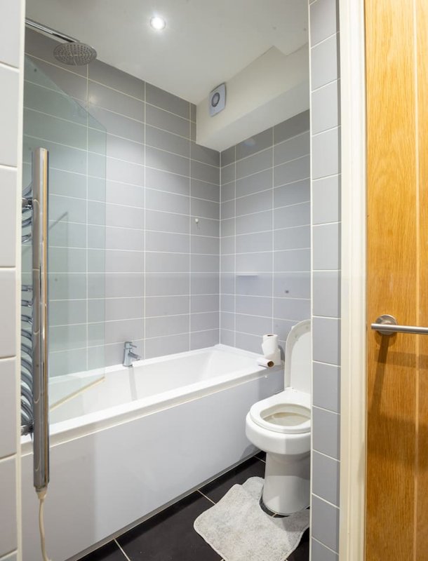 Modern bathroom with white bathtub, grey tile walls, heated towel rail, and toilet