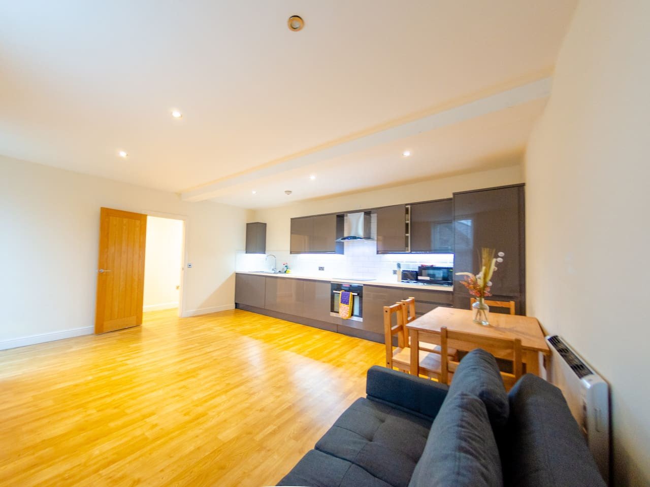 Open-plan living area with wooden flooring, modern kitchen, sofa and dining table