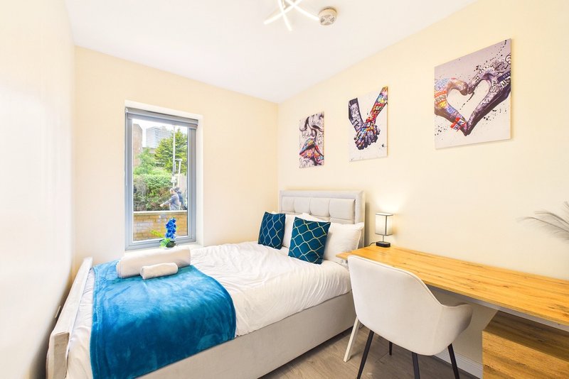 Bright bedroom with single bed, blue bedding, wooden desk, window view and wall art